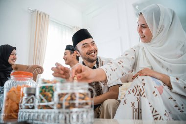 Muslim couple chatting while taking snacks from a jar during a visit to celebrate Eid at a friends house