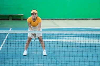 Asian female tennis player in ready position holding racket on tennis court