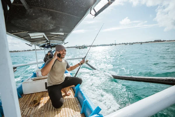 angler making a cell phone call while holding a fishing rod on a small fishing boat