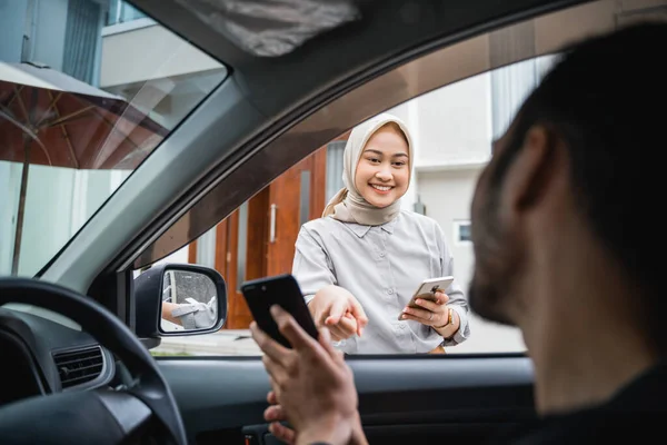 Asian veiled woman points at transportation drivers cell phone when he comes to pick her up
