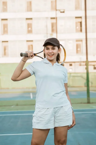 Asian female tennis athlete holding racket on shoulders while standing on court