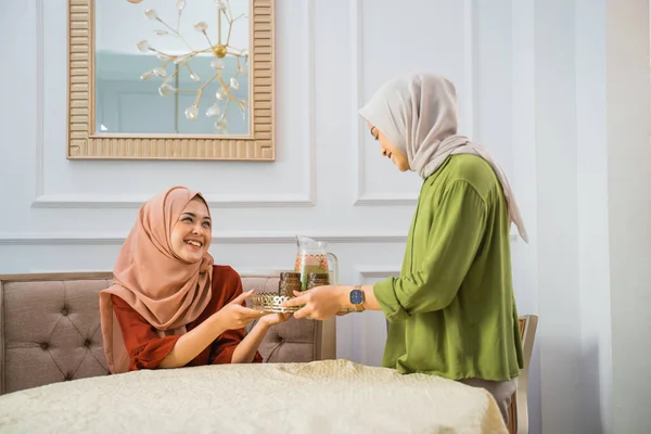 Asian woman in hijab serves drinks when her friend visits her home