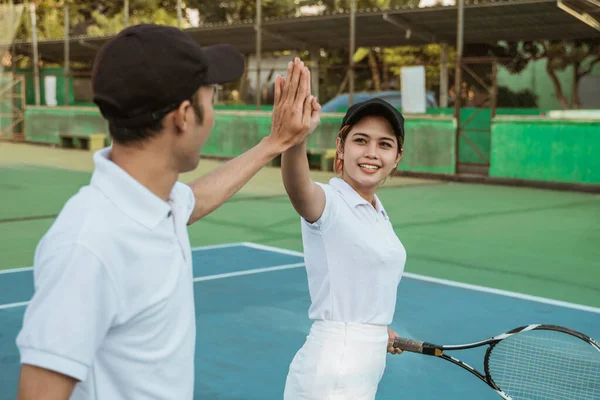 Mixed doubles tennis athletes high-five each other celebrating victory while playing on the tennis court