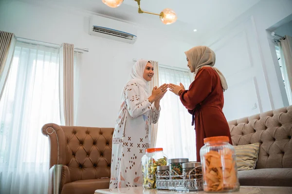 two Muslim women in hijabs greeting Eid while standing in the background of the living room
