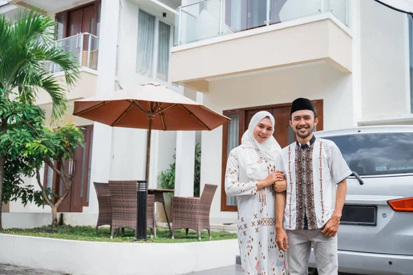 Asian Muslim husband and wife smiling with joined hands standing in front of the house