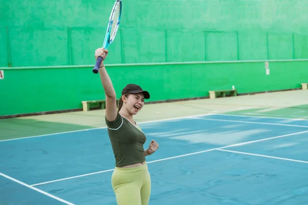 female tennis player winning fist clenched and lifting tennis racket on tennis court