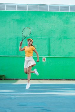 Female tennis player moving in jumping after hitting ball with racket on tennis court