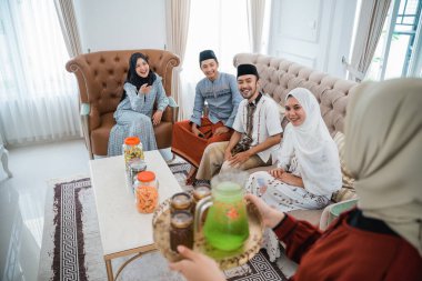 group of Muslim friends are happy when a veiled woman brings a drinking tray to be served during the Eid celebration together at home