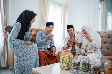 two Muslim couples laughing using cellphones together while celebrating Eid at home