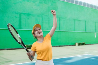 happy tennis player with clenched hand gesture after hitting the ball to score with racket on tennis court