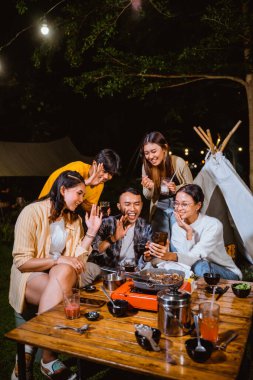 a group of people video calling with someone on phone while hangout together at the camp site