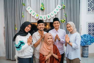 a group of young Muslims with hand gestures congratulate Eid while celebrating Eid at home