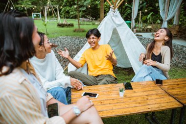 a guy in yellow t shirt laughing and open his hands while chatting with his friends at camp site