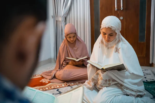 women participants wearing white hijab reciting the Quran following the male recitation leader in the room