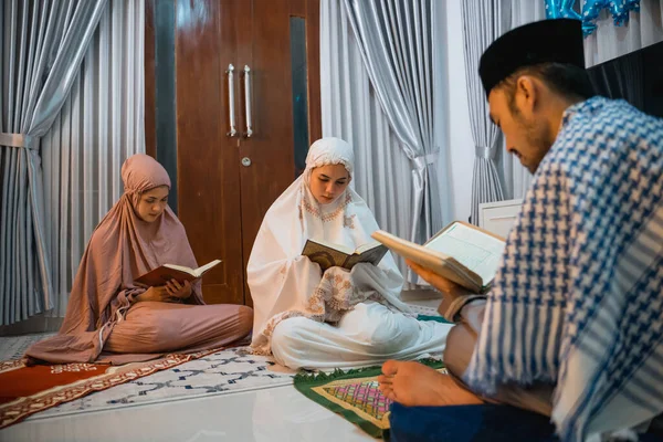 two women participants wearing hijab read the Quran following male recitation leader at home