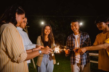 a group of people playing with the fireworks happily and standing in circle while camping at the camp site