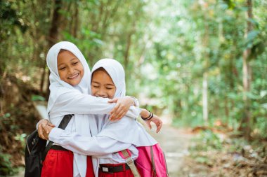 Üniformalı iki güzel ilkokul öğrencisi köy yolunda yan yana durur ve birbirlerine sarılırlar.