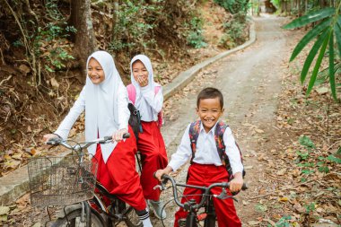 Üç ilkokul öğrencisi birlikte kır yolunda bisiklet sürüyorlar.