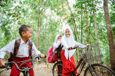 Üniformalı üç ilkokul öğrencisi Country Road 'da bisikletlerini durdurup birlikte gülümsüyorlar.