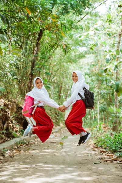 Dwie Uczennice Elementarne Mundurze Skaczące Szczęśliwie Wiejskiej Drodze Dłonią Dłoni — Zdjęcie stockowe