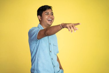 Asyalı genç bir adamın portresi, izole edilmiş arka planda parmakla işaret ederek gülüyor.