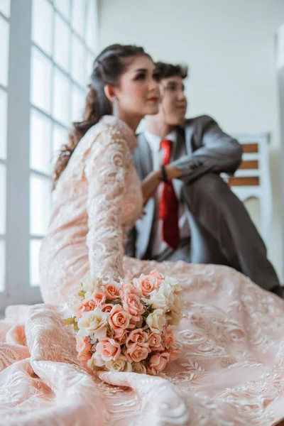 亚洲新娘坐在新郎旁边的地板上 手里拿着花束 — 图库照片
