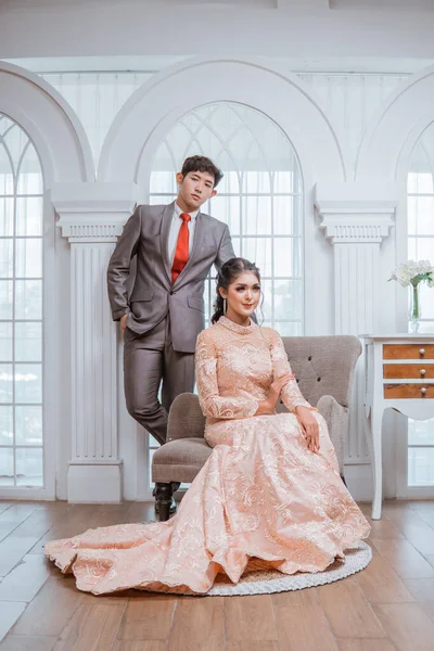 Asiatisk Brud Orange Klänning Sitter Stolen Medan Brudgummen Står Bakom — Stockfoto