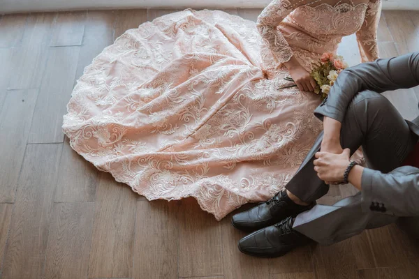 身穿橙色长袍的新娘与身穿灰色西服的新郎一起坐在地板上 — 图库照片