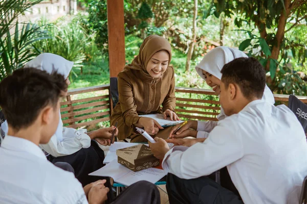 学生時代のスカーフ姿のアジア人教師は屋外授業で本を使って課題に取り組み — ストック写真