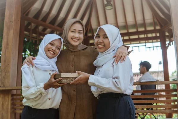 ヒジャーブの女性教師と2人の女性学生が屋外でプレゼントをしながら笑顔で — ストック写真