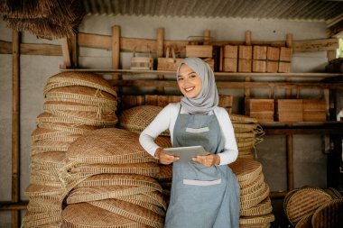 Geleneksel bambu ürünleri dükkanında elinde tablet tutan Asyalı Müslüman kadın.