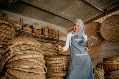 Çekici Müslüman kadın, online dükkandaki geleneksel bambu ürünlerini kontrol etmek için tablet kullanıyor.
