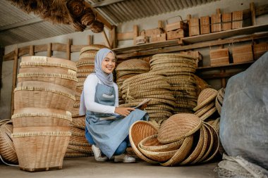 Çekici Müslüman kadın, online dükkandaki geleneksel bambu ürünlerini kontrol etmek için tablet kullanıyor.