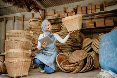 Çekici Müslüman kadın, online dükkandaki geleneksel bambu ürünlerini kontrol etmek için tablet kullanıyor.