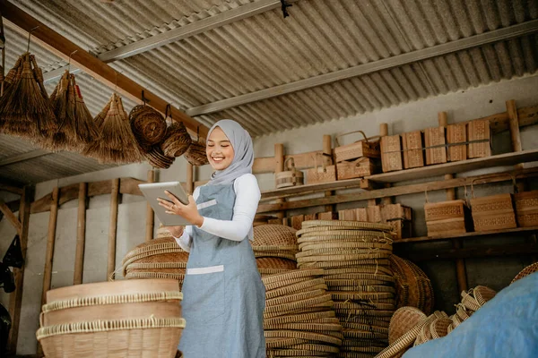 アジア系ムスリム女性の伝統的な竹製品店でタブレットPcを持っています — ストック写真
