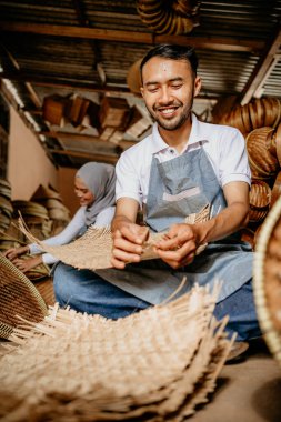 Mutlu Asyalı el sanatları ustası dükkânda dokuma bambu ürünleri üzerinde çalışıyor.