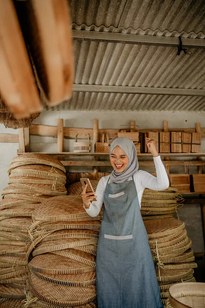 Heyecanlı genç Müslüman bayan girişimci cep telefonunu kullanırken elini kaldırdı