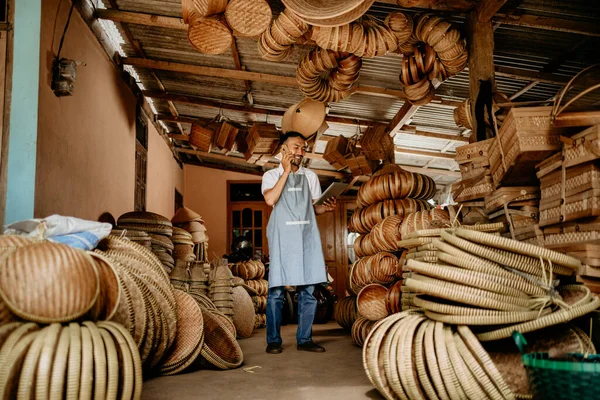 Genç Asyalı erkek zanaat sahibi deposunda çalışırken telefonla konuşuyor.