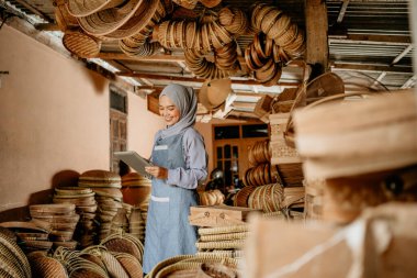 Çekici Müslüman kadın, online dükkandaki geleneksel bambu ürünlerini kontrol etmek için tablet kullanıyor.