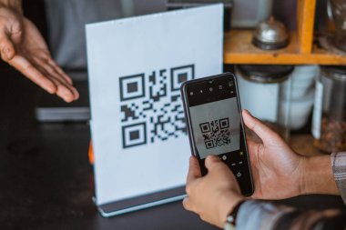 Telefon kullanarak qr kodunu tarayan bir müşterinin eli