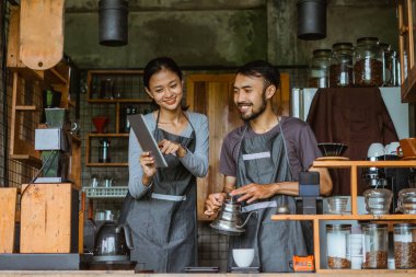 Kadın baristanın tuttuğu dijital tablete bakarken erkek barista kahve yapıyor.