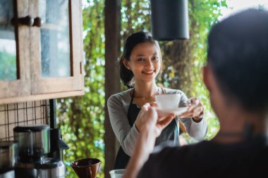 Kahveyi kadın kahveciye verirken erkek barista gülümsüyor.