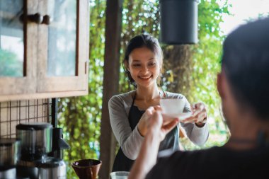 Kahveyi kadın kahveciye verirken erkek barista gülümsüyor.