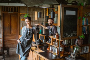 Kadın bir barmen elini cebine sokup barın masasında dikilen erkek kahveci...