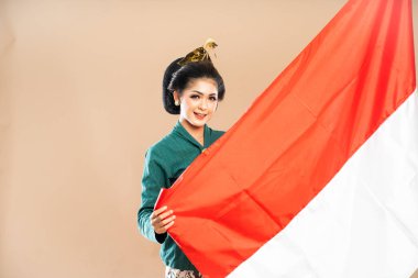 Yeşil kebaya giymiş Asyalı kadın gülümseyerek dikilirken izole edilmiş arka planda Endonezya bayrağını tutuyor.