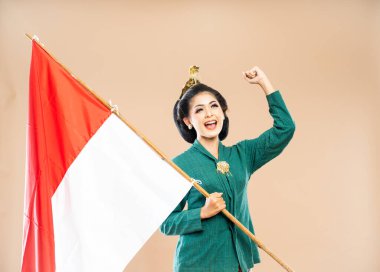 Yeşil kebaya giymiş gülümseyen Asyalı kadın kollarını sımsıkı tutmuş ve izole edilmiş arka planda Endonezya bayrağını tutuyor.