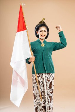 Yeşil kebaya giymiş Asyalı kadın kollarını sımsıkı tutmuş ve izole edilmiş arka planda Endonezya bayrağını tutuyor.