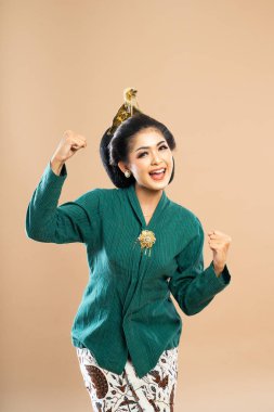 Yeşil kebaya giymiş mutlu Asyalı kadın kollarını izole edilmiş arka planda eğiyor ve sıkıyor.