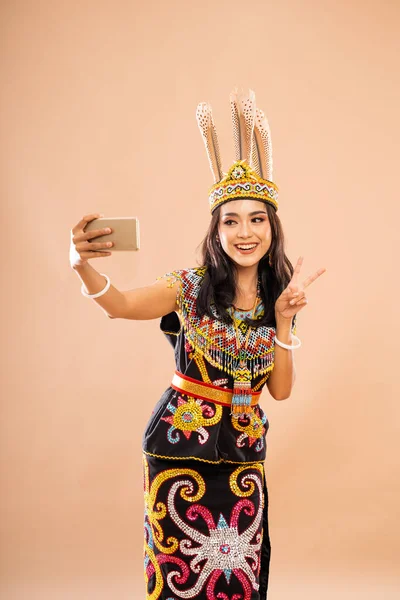 平和の手のジェスチャーと笑顔で立ち並ぶアジア系女性が孤立した背景で携帯電話を使って自撮り写真を撮る — ストック写真