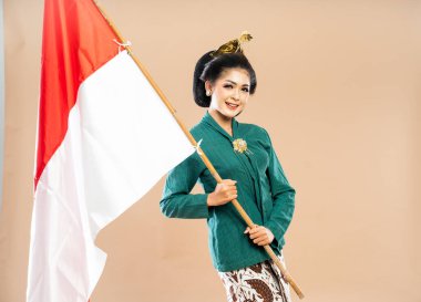 Yeşil kebaya giymiş gülümseyen Asyalı kadın izole edilmiş arka planda Endonezya bayrağını tutuyor.